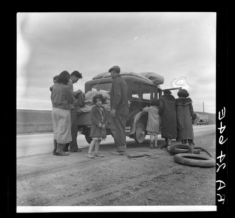 A family on the side of the road, gathered around a car and their luggage