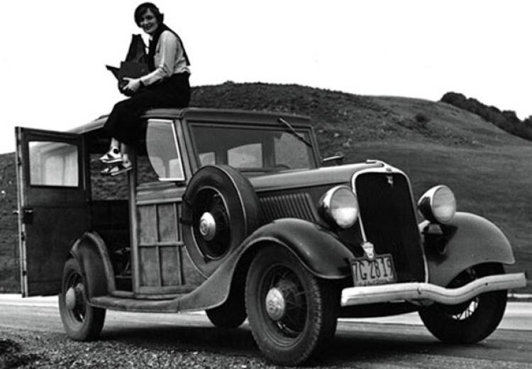 Photographer Dorothea Lange takes a break on top of a car