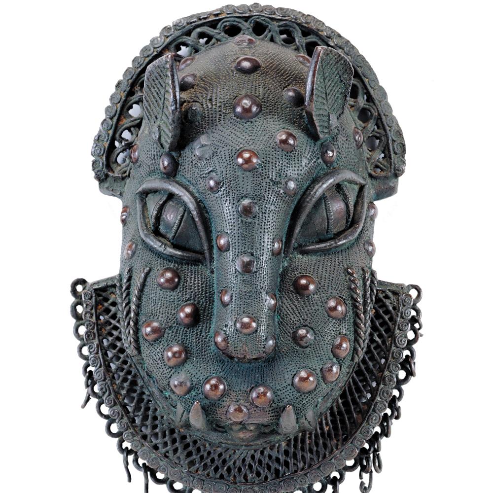 Blue green brass ornament in the shape of a leopard head, with brass studs decorating the face