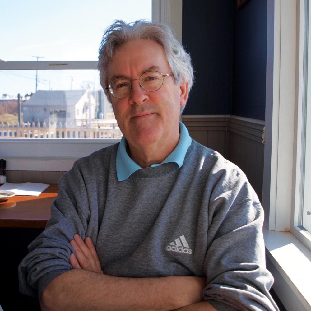 Color photo of Wayne Miller wearing a grey sweatshirt and teal polo shirt underneath.