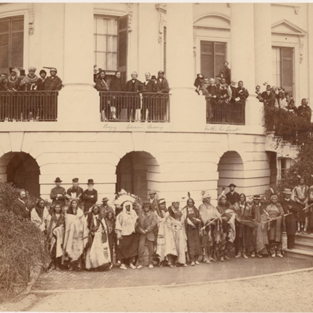 Sepia-colored photo of a large Native American delegation standing in front of the White House.