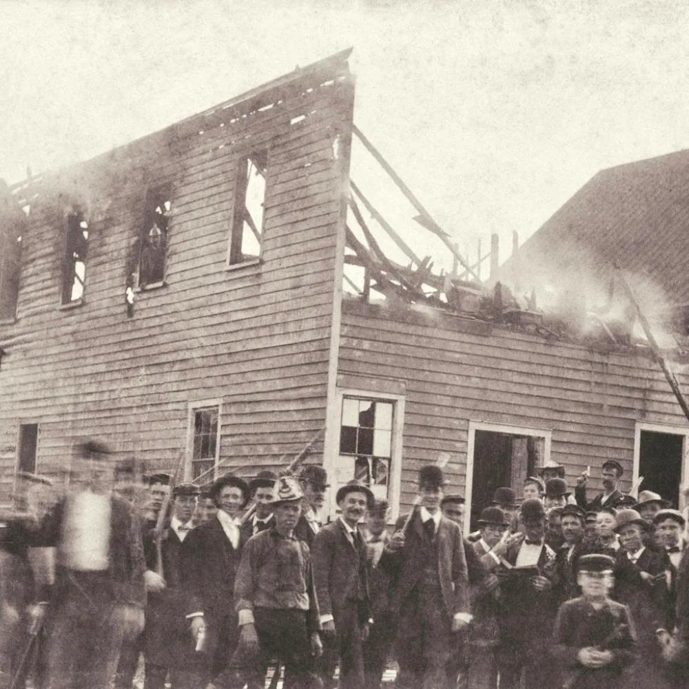 black and white photograph of mob in front of burning building.