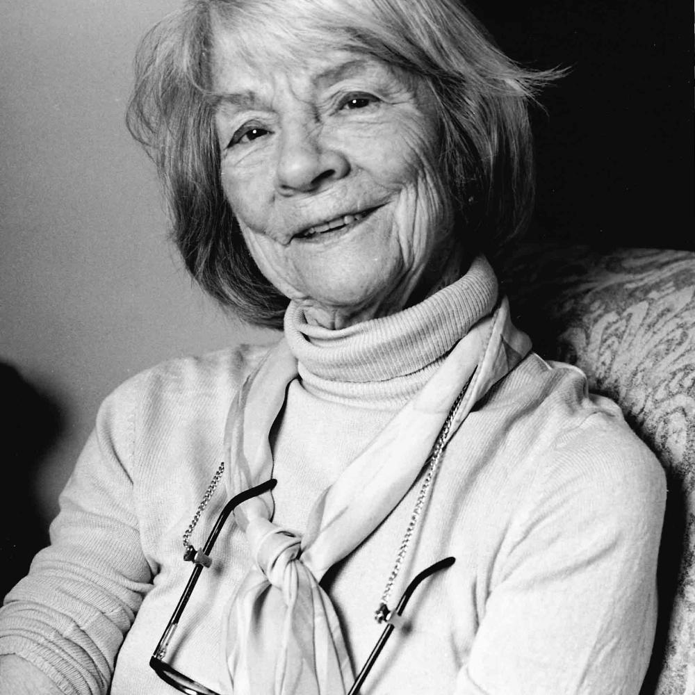 Black-and-white photo of Judith Jones late in life sitting in a chair with her glasses slung around her neck.