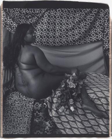 Black woman with back turned and face in profile lounges on patterned fabric