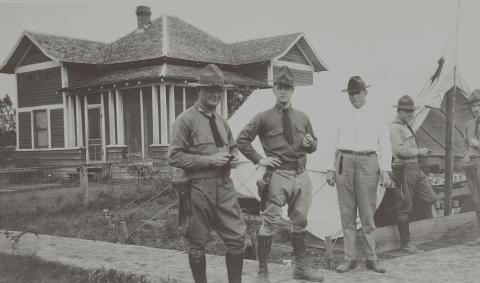 Black and white photograph of four men in uniforms standing in front of a building
