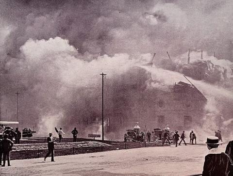 Cloud of smoke engulfing a building, with onlookers and firefighters in the foreground