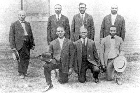Black and white photograph of seven Black men in suits, four standing and three kneeling