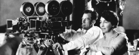 Black and white photo of filmmaker Lois Weber, seated behind camera with man