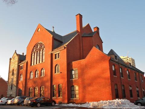 Color photo of red brick church with cars and shoveled snow in parking lot