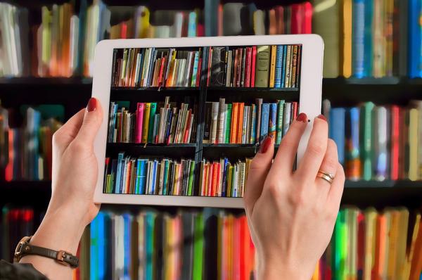 Two hands holding up a tablet in front of a large bookshelf