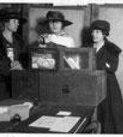 Three women in hats placing their votes at a ballot box