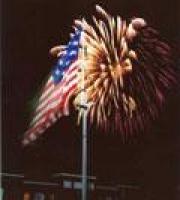 American flag flying on a pole, with a night sky lit up by fireworks in the background