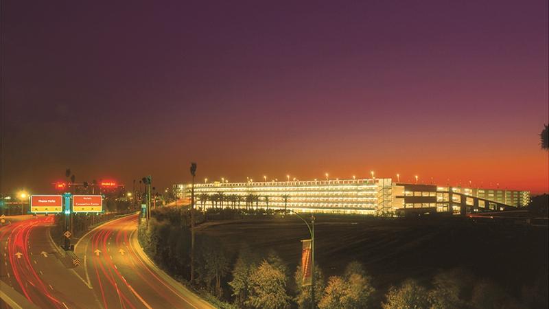 Photograph of a parking structure in distance, highway in foreground, at sunset