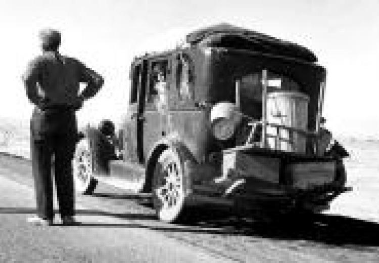 Migrant, standing with hands on hips and back to the viewer, next to his stalled truck