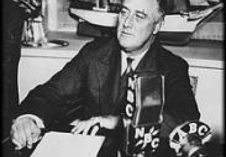 FDR sitting at his desk with notes and microphones in front of him