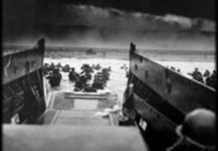 Black and white photo of soldiers exiting a landing craft onto the beaches at Normandy, France.