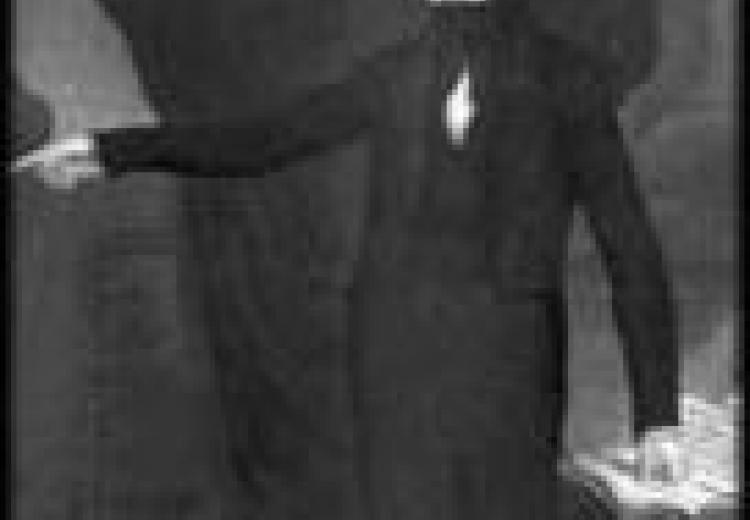 Clay in a dark suit, raising his arm and pointing