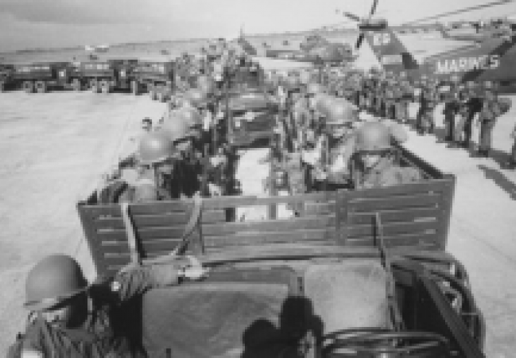 a line of military transport trucks, carrying troops in helmets