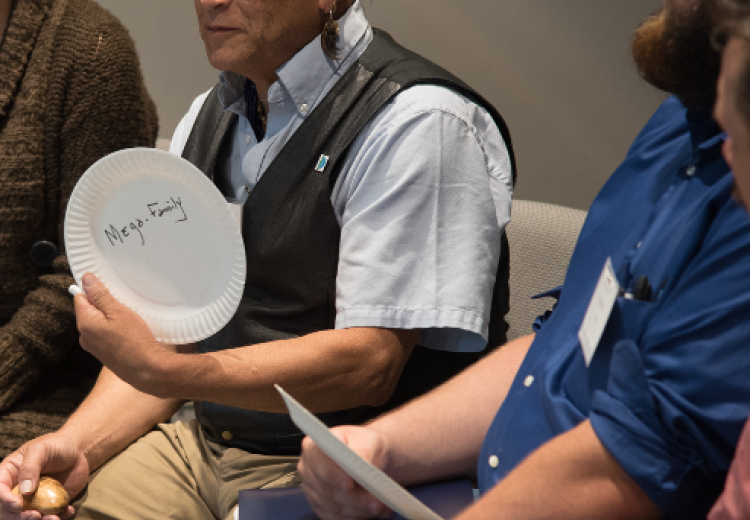 Three people sitting, with the main focus being on one person sharing a thought; and a paper plate saying "Mega-Family"