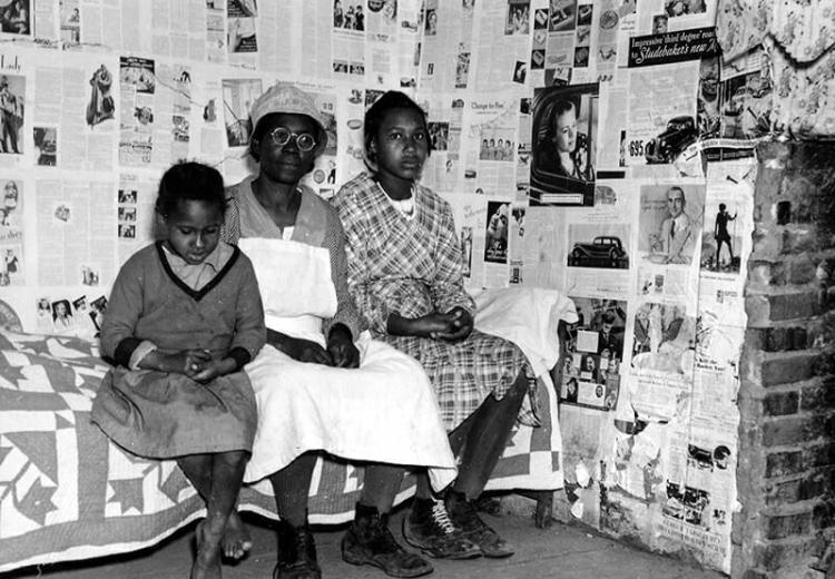 Three women of differing ages seated on bed, facing camera